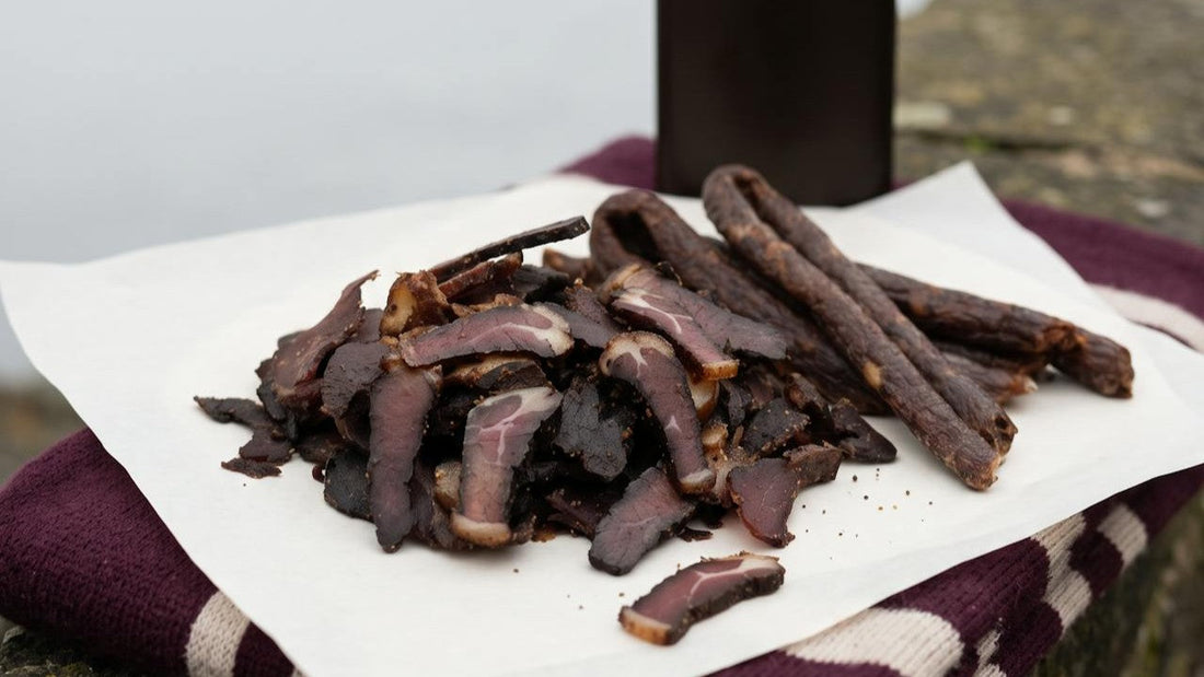 Sliced biltong and droëwors on butcher's paper over a damson scarf, ready for match day